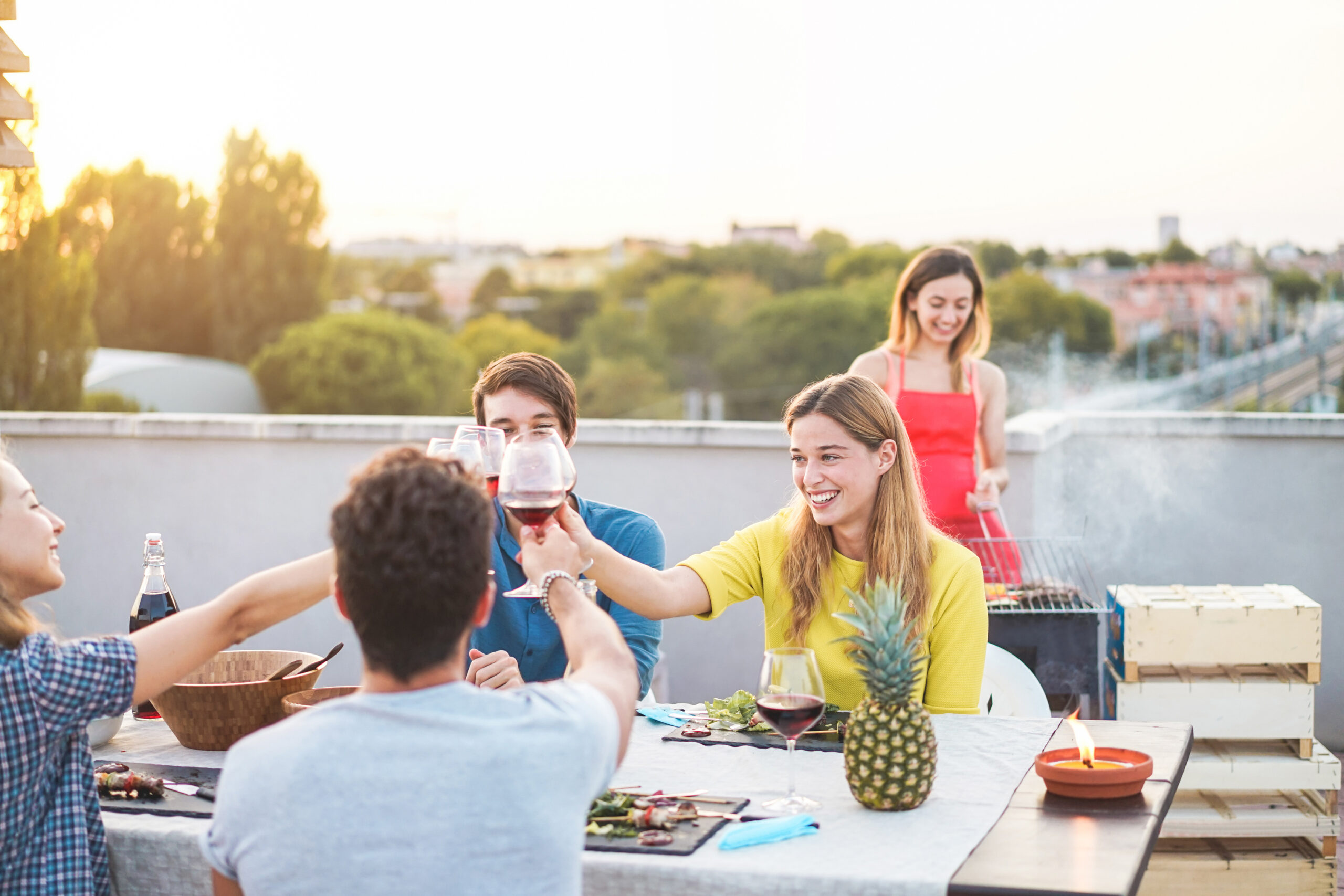 Young friends having barbecue party at sunset on penthouse patio - Happy people doing bbq dinner outdoor cooking meat and drinking wine - Focus on right woman - Food, fun and friendship concept